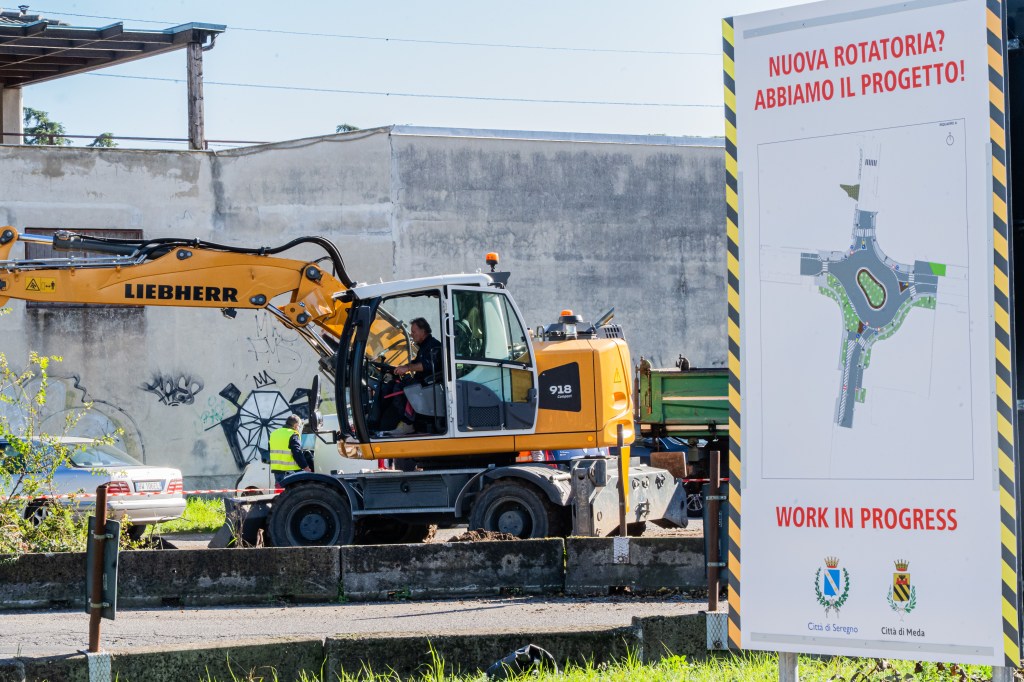Operai al lavoro nel cantiere. Nell'immagine è visibile anche il progetto della nuova rotatoria, esposto su un cartellone informativo dei comuni di Seregno e Meda. 
