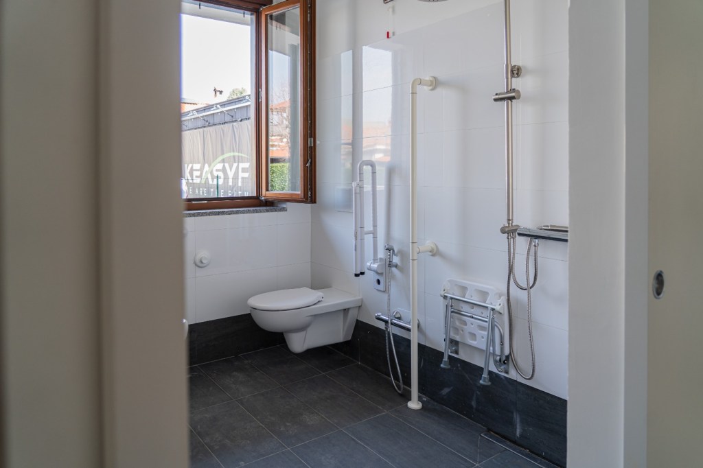Immagine di uno dei bagni dell'appartamento al piano terreno destinato all'accoglienza delle persone con disabilità. Il bagno ha una doccia e dei sanitari attrezzati per le persone con disabilità motorie.