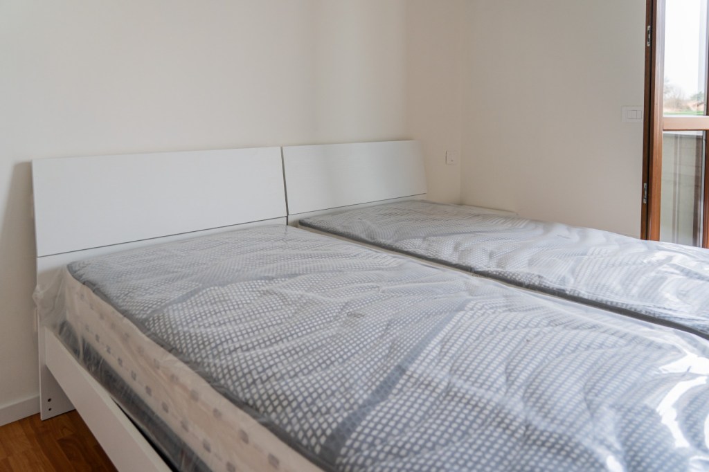 Immagine raffigurante un letto matrimoniale dotato di due materassi singoli all'interno di una stanza in uno degli appartamenti destinati ad housing sociale.